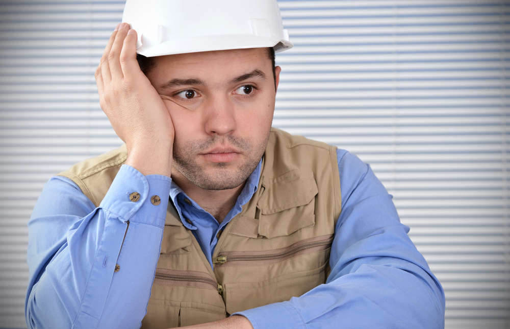 Man in hard hard hat with his hand on his face looking upset